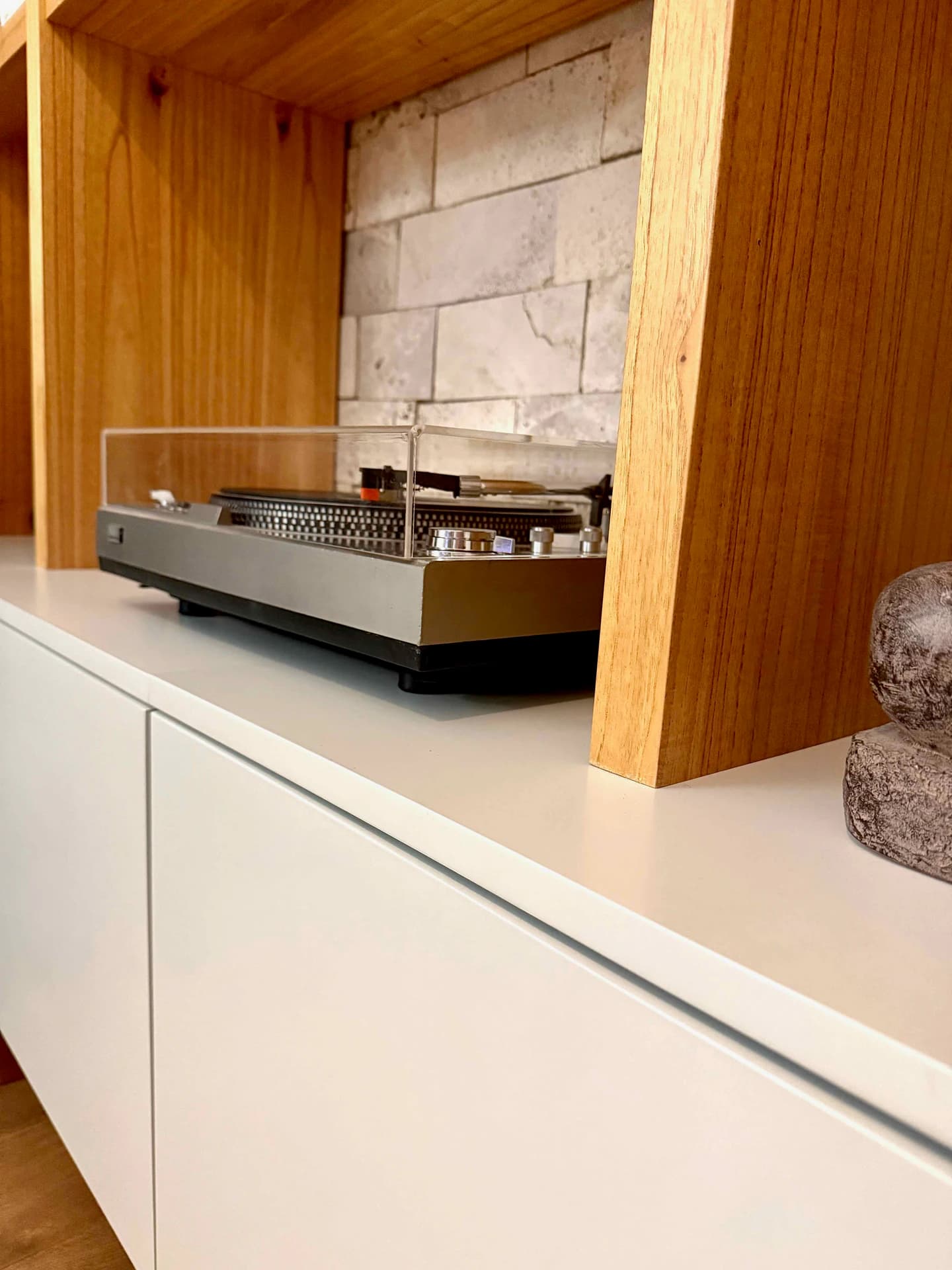 Detalle de las divisiones color madera y las puertas inferiores blancas de la biblioteca, con un tocadiscos sobre la superficie de apoyo.