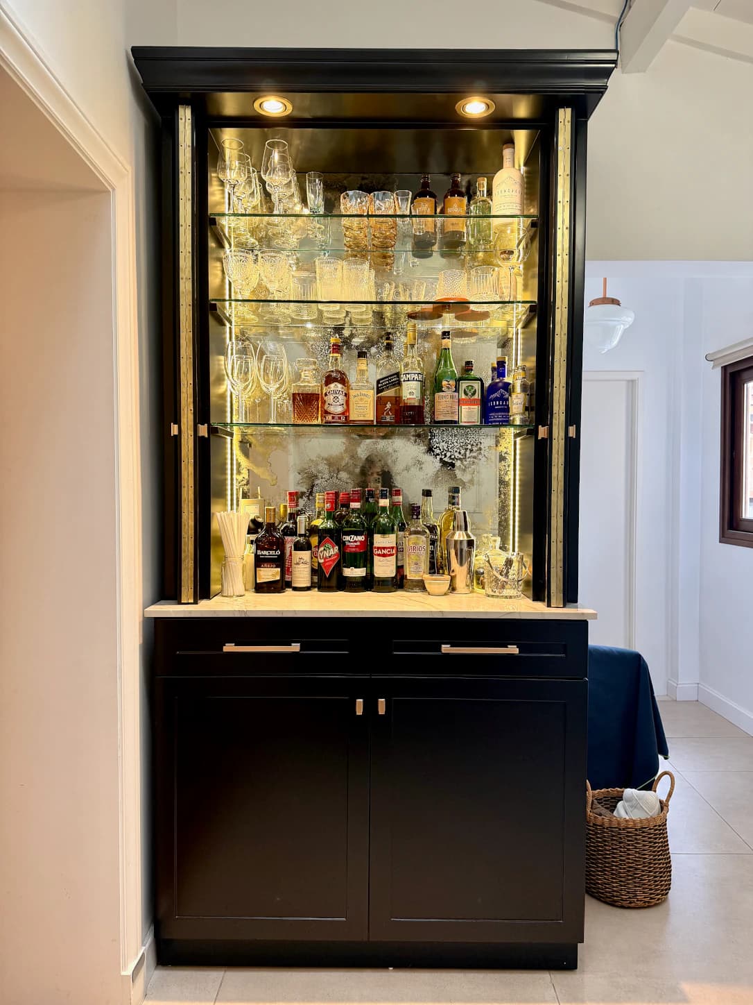 Vista frontal del mini bar abierto, con estantes para copas, superficie de apoyo, cajones y puertas inferiores.
