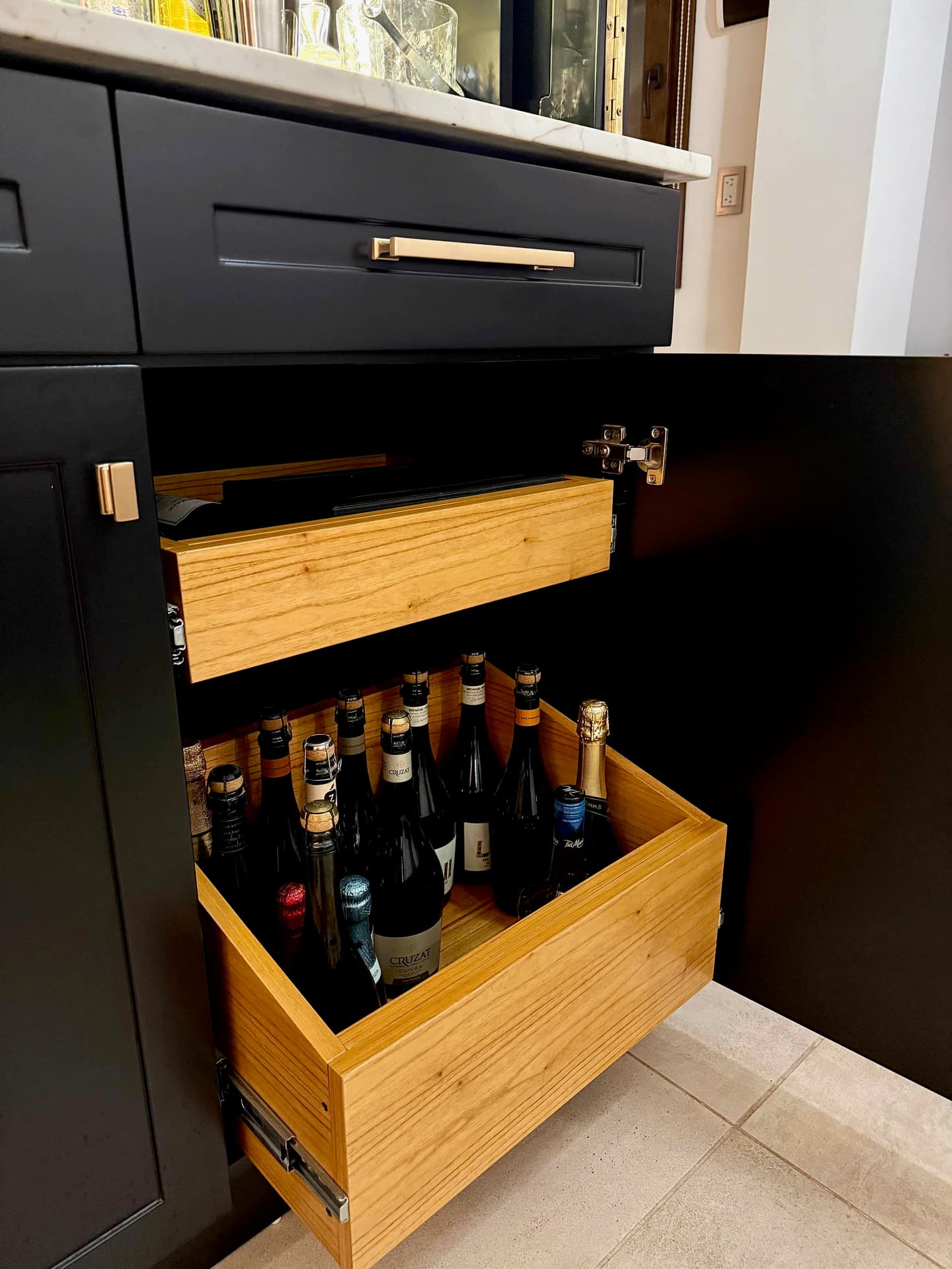 Cajones interiores de MDF enchapado en Paraíso abiertos, con botellas en el cajón inferior del mini bar.