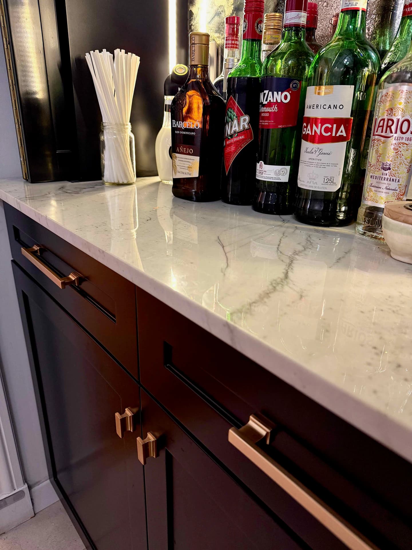 Detalle de los frentes oscuros y sus tiradores bajo la superficie de apoyo del mini bar, con los cajones cerrados.